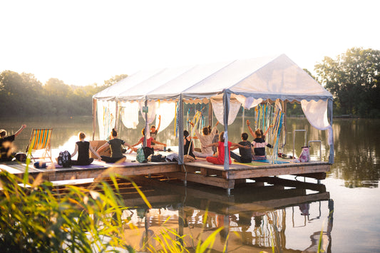 A group of people is participating in a yoga class on a floating platform on a serene lake at sunset