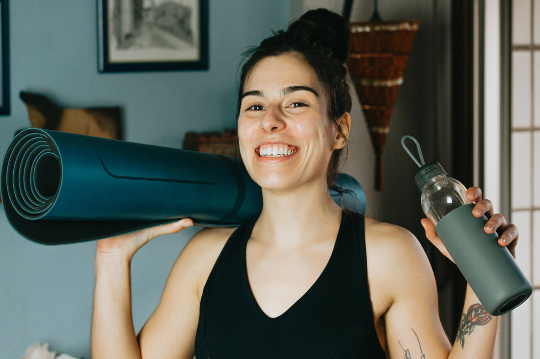a-woman-smiles-holding-a-water-bottle-and-a-yoga-mat