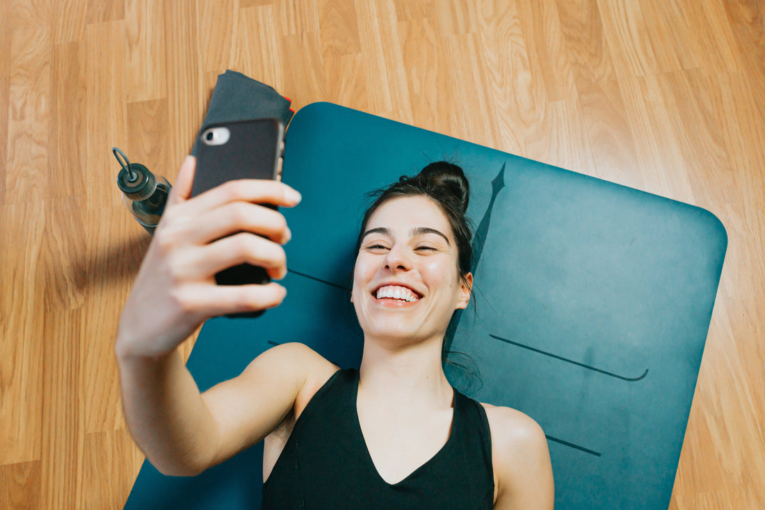 person-on-a-yoga-mat-smiles-at-their-cell-phone