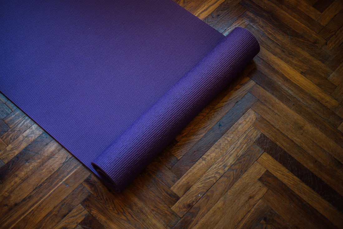 purple-yoga-mat-partially-rolled-on-a-wooden-floor