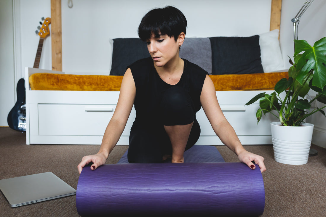 woman-rolls-purple-yoga-mat-onto-living-room-floor