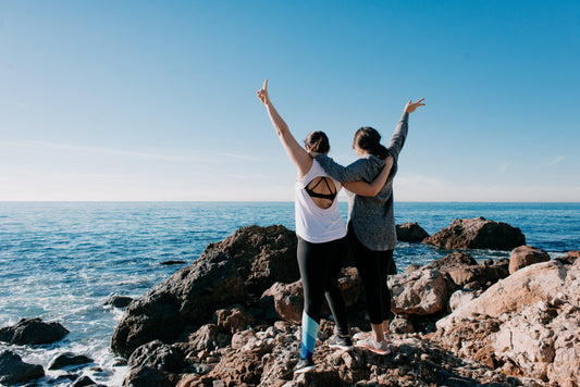 women-arm-in-arm-raise-their-hands-in-peace-sign-on-beach