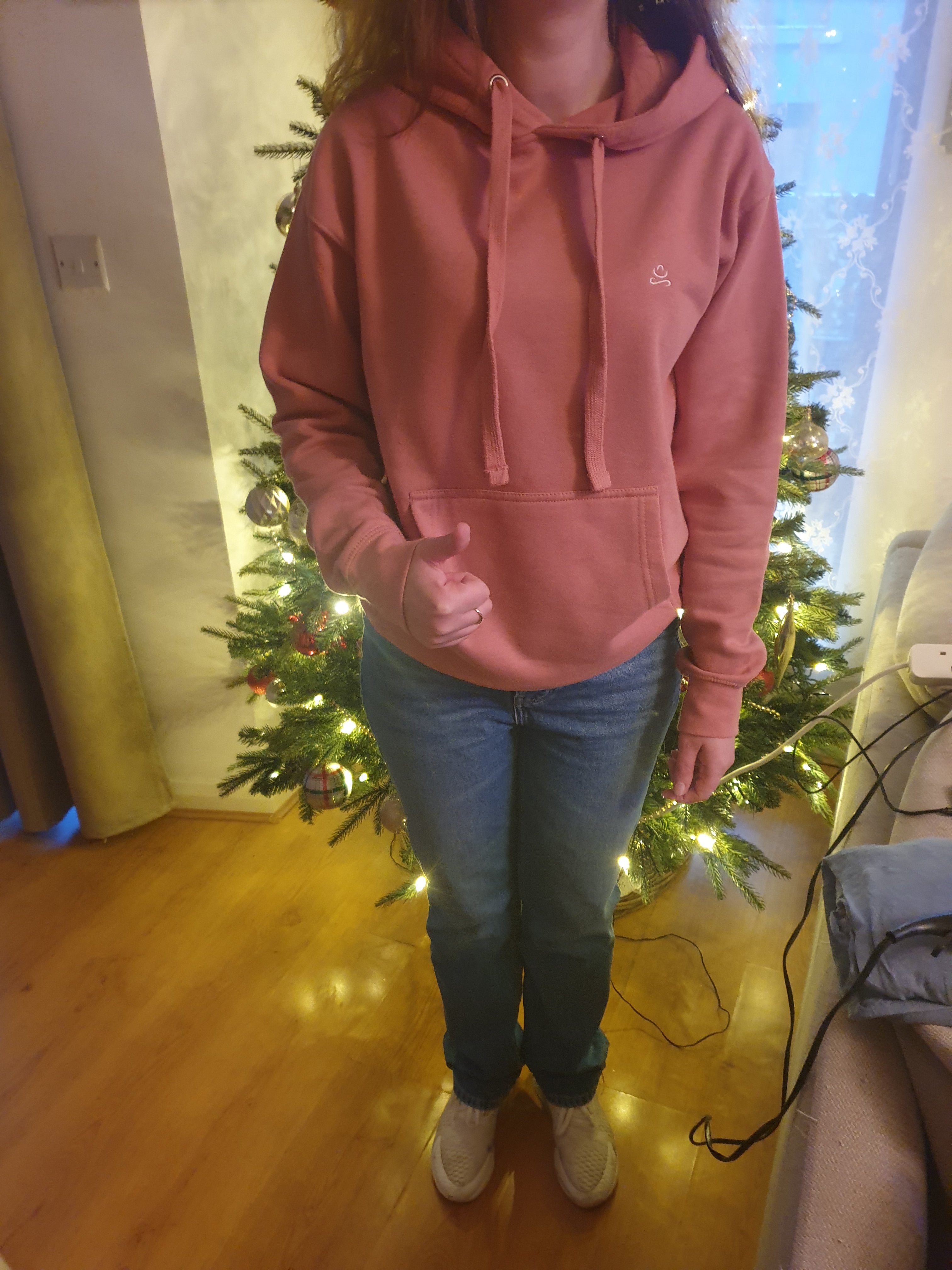 Woman standing if the room wearing pink hoodie from jain yoga brand showing satisfaction with her purchase