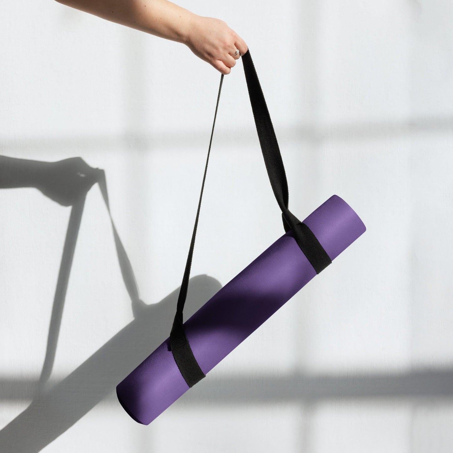 Yoga mat held n the air using straps in front of white wall casting shadow